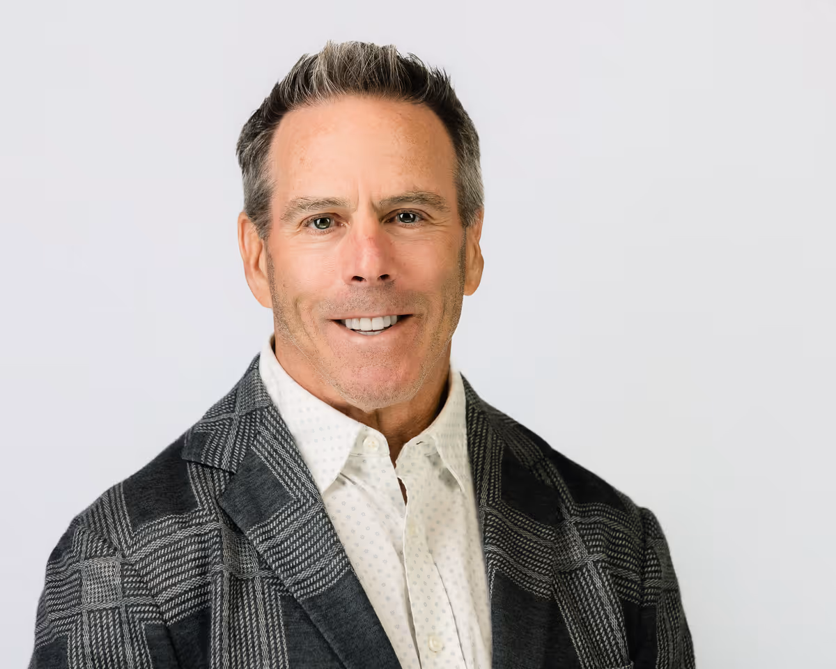 Smiling middle-aged man with short gray hair wearing a patterned gray blazer over a white button-up shirt.